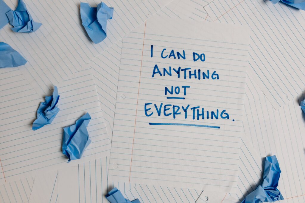 Pieces of paper scattered in a pile including some pieces that are screwed up. One piece of paper says 'I can do anything not everything'