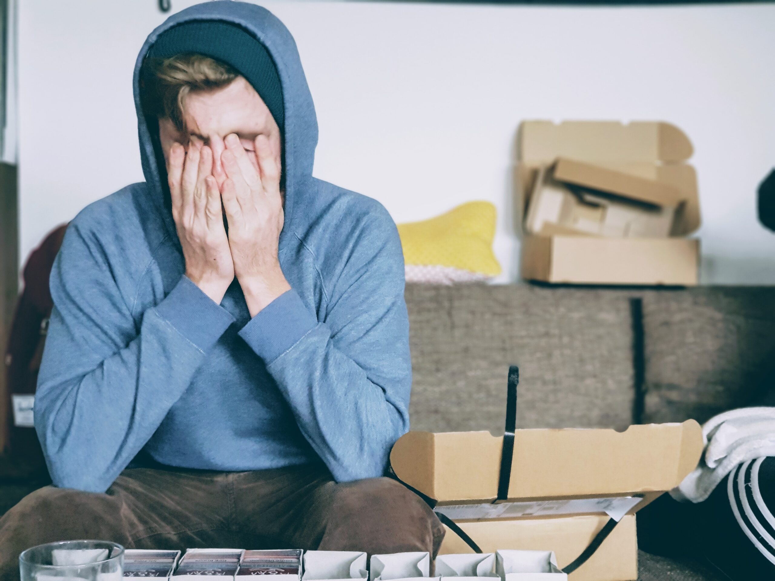 Man in hoody is sat down with hands across his face as if he is exhausted or upset