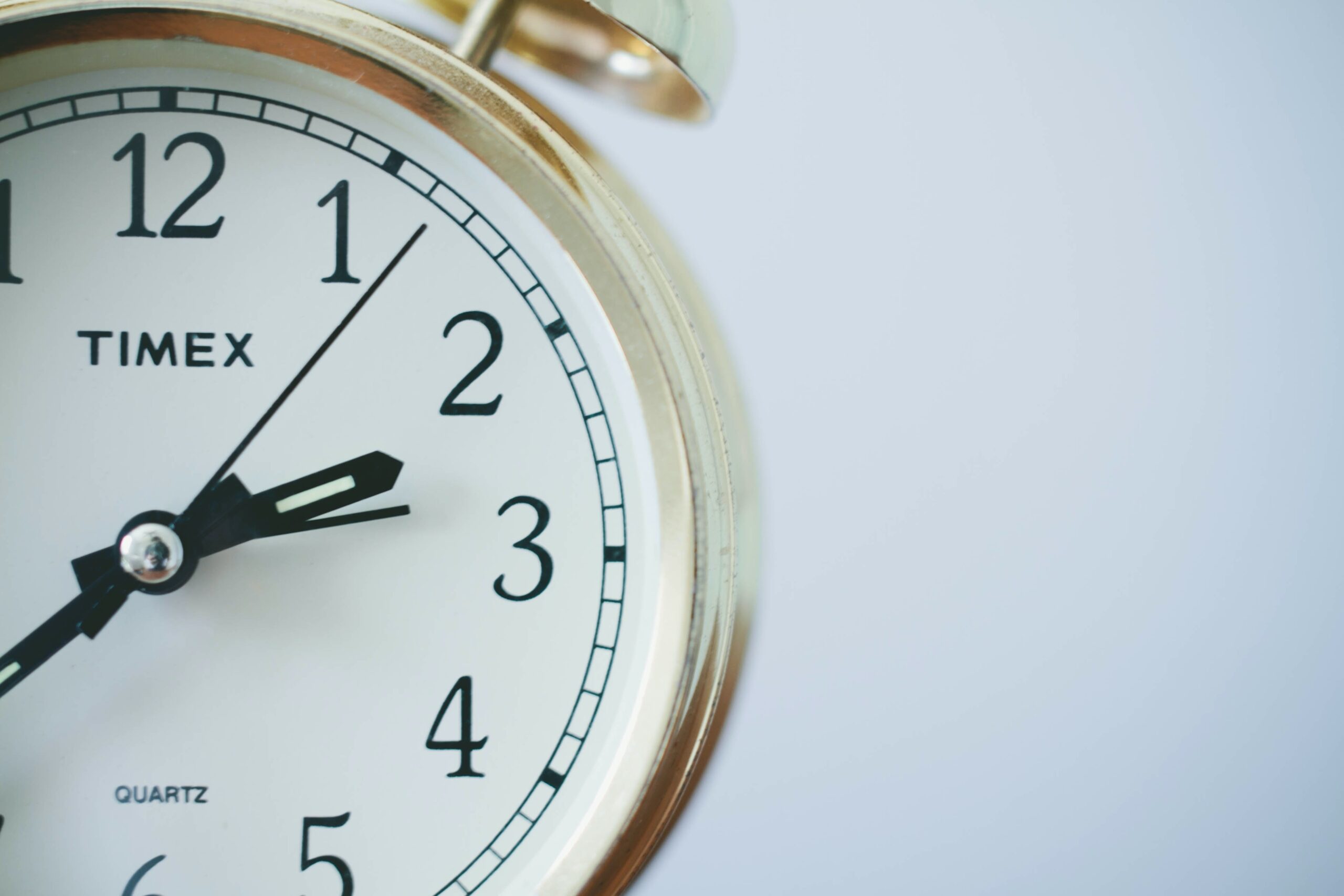 Alarm clock with a gold case and gold bells at the top, a white face, and black numbers and clock hands