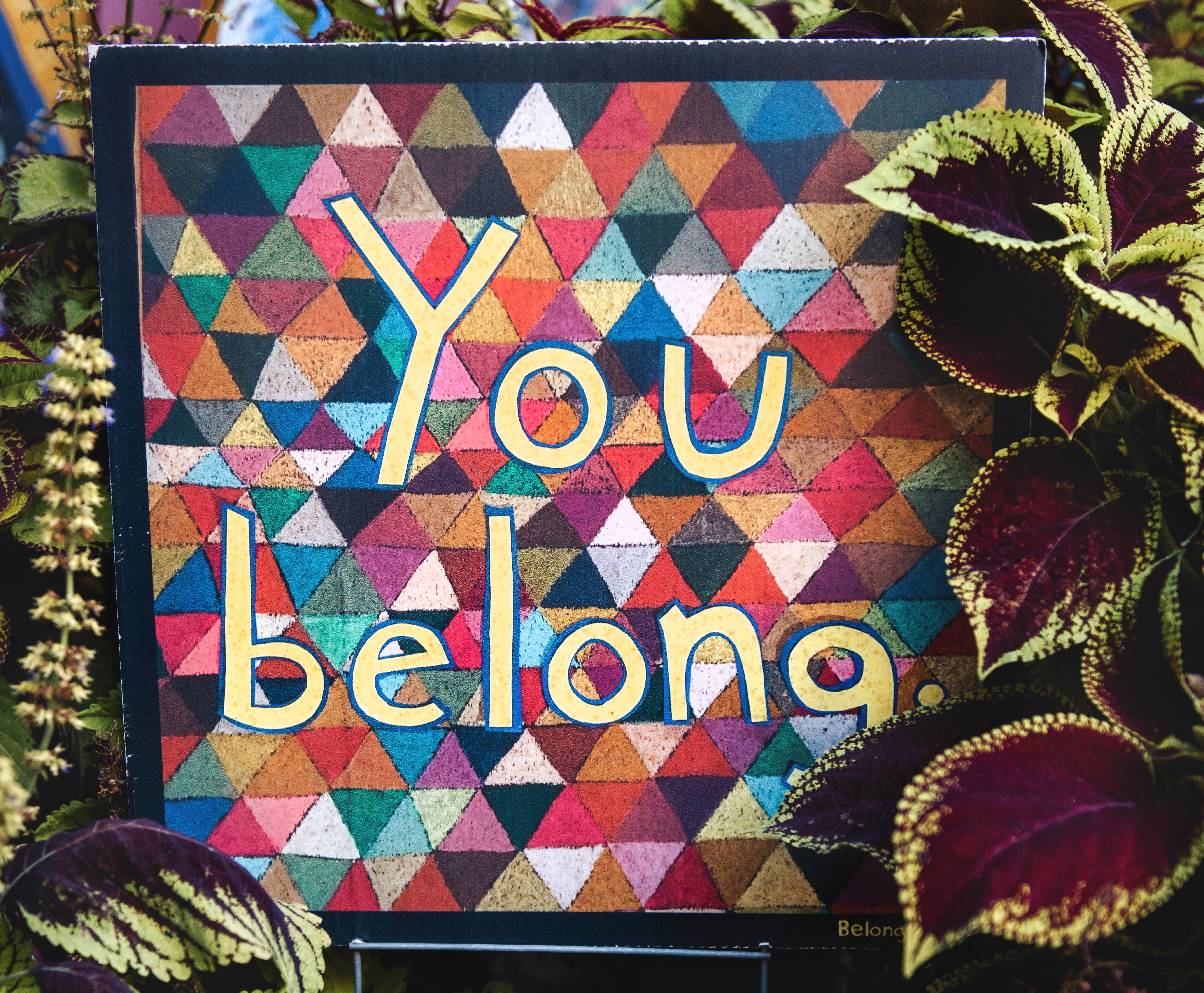 a mosaic style artwork with triangles in different colours with the words You Belong painted on in a handwriting style
