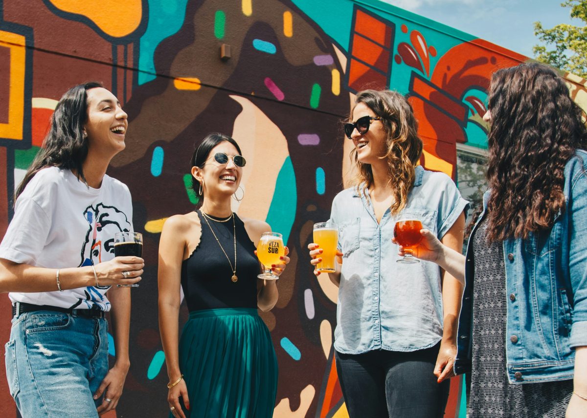 A group of women enjoying drinks in the sunshine beside a colourful painted wall
