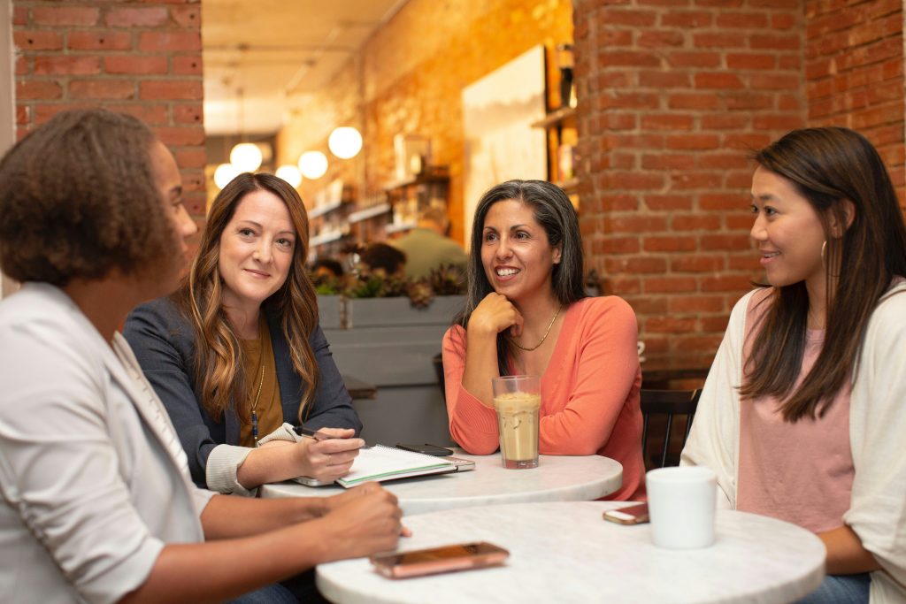 A group of women in work clothing (blazers and shirts) sitting at a table having a discussion